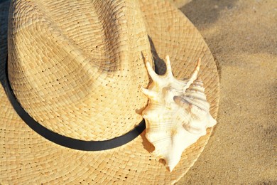 Photo of Stylish straw hat and sea shell on sandy beach, closeup