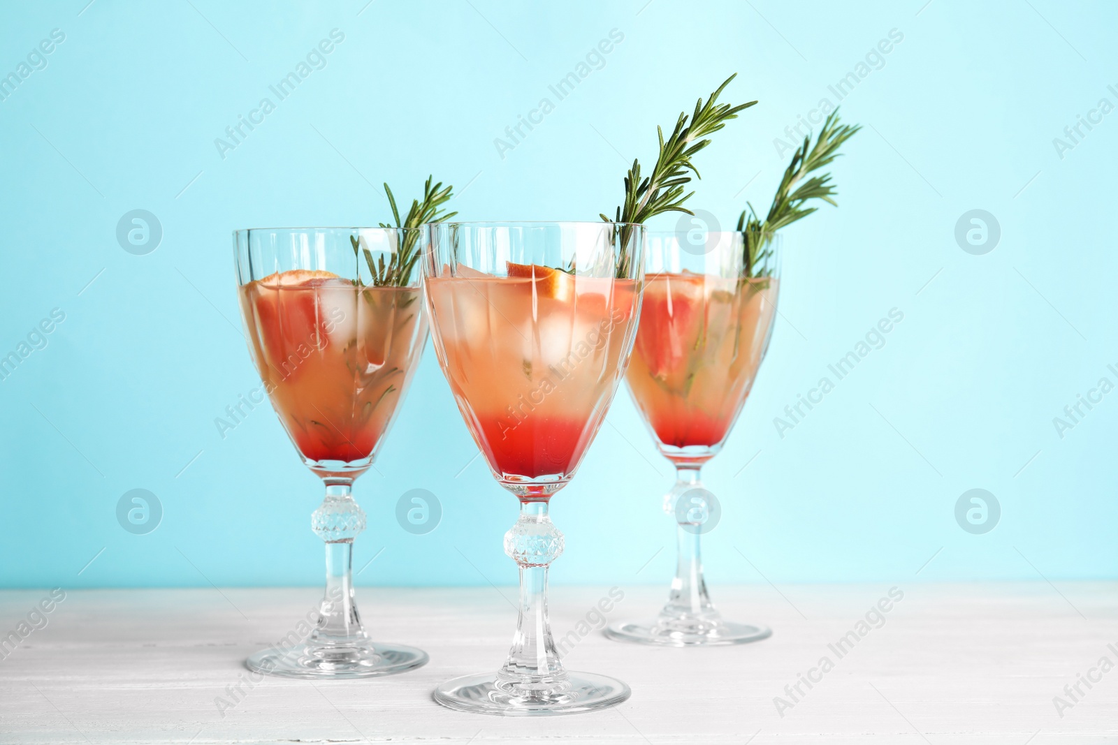 Photo of Glasses of grapefruit cocktails on table against color background