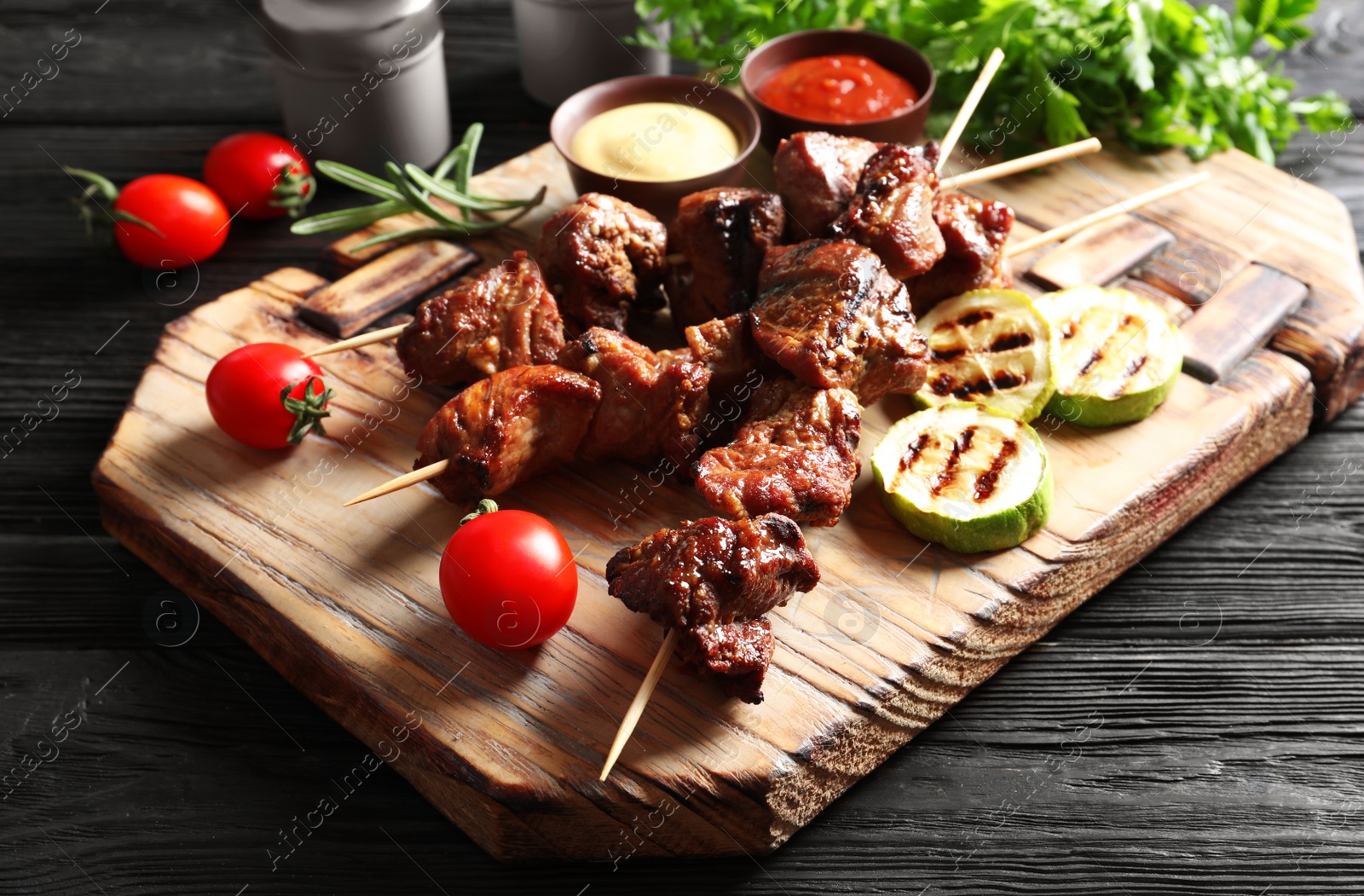 Photo of Delicious barbecued meat served with garnish and sauces on wooden board