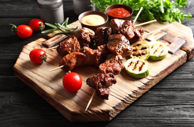 Photo of Delicious barbecued meat served with garnish and sauces on wooden board