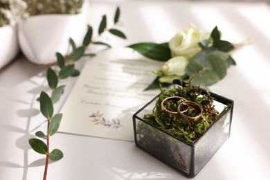 Photo of Beautiful wedding rings in glass box, boutonniere and invitation on white background