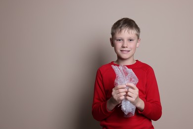 Photo of Happy boy popping bubble wrap on beige background, space for text. Stress relief