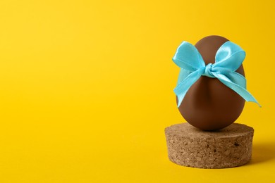Photo of Tasty chocolate egg with light blue bow on orange background. Space for text