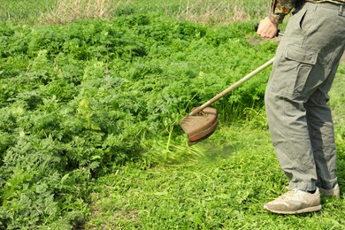 Photo of Worker cutting grass with electric lawn trimmer outdoors, closeup