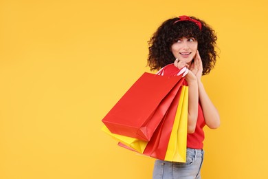 Happy young woman with shopping bags on yellow background. Space for text