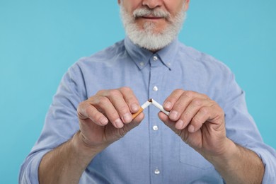 Stop smoking concept. Man breaking cigarette on light blue background, closeup