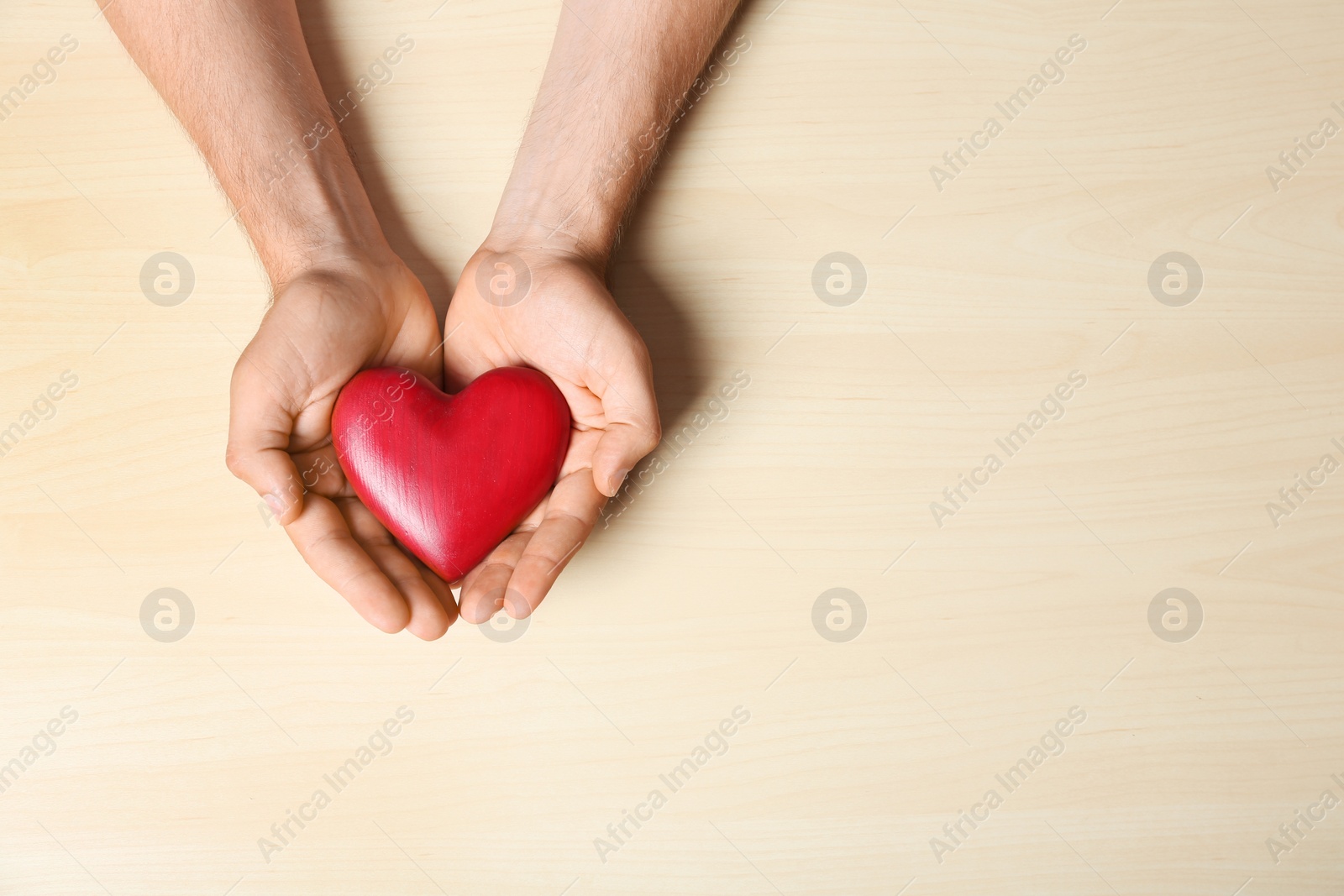 Photo of Young man holding red heart on light wooden background, top view with space for text. Donation concept