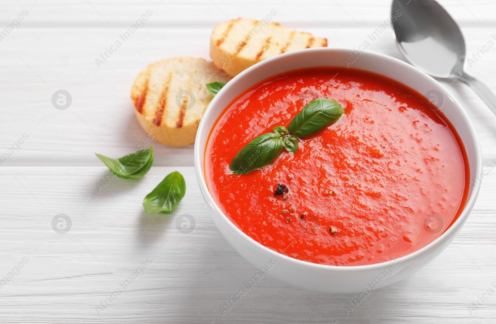 Photo of Delicious tomato cream soup in bowl on white wooden table, space for text