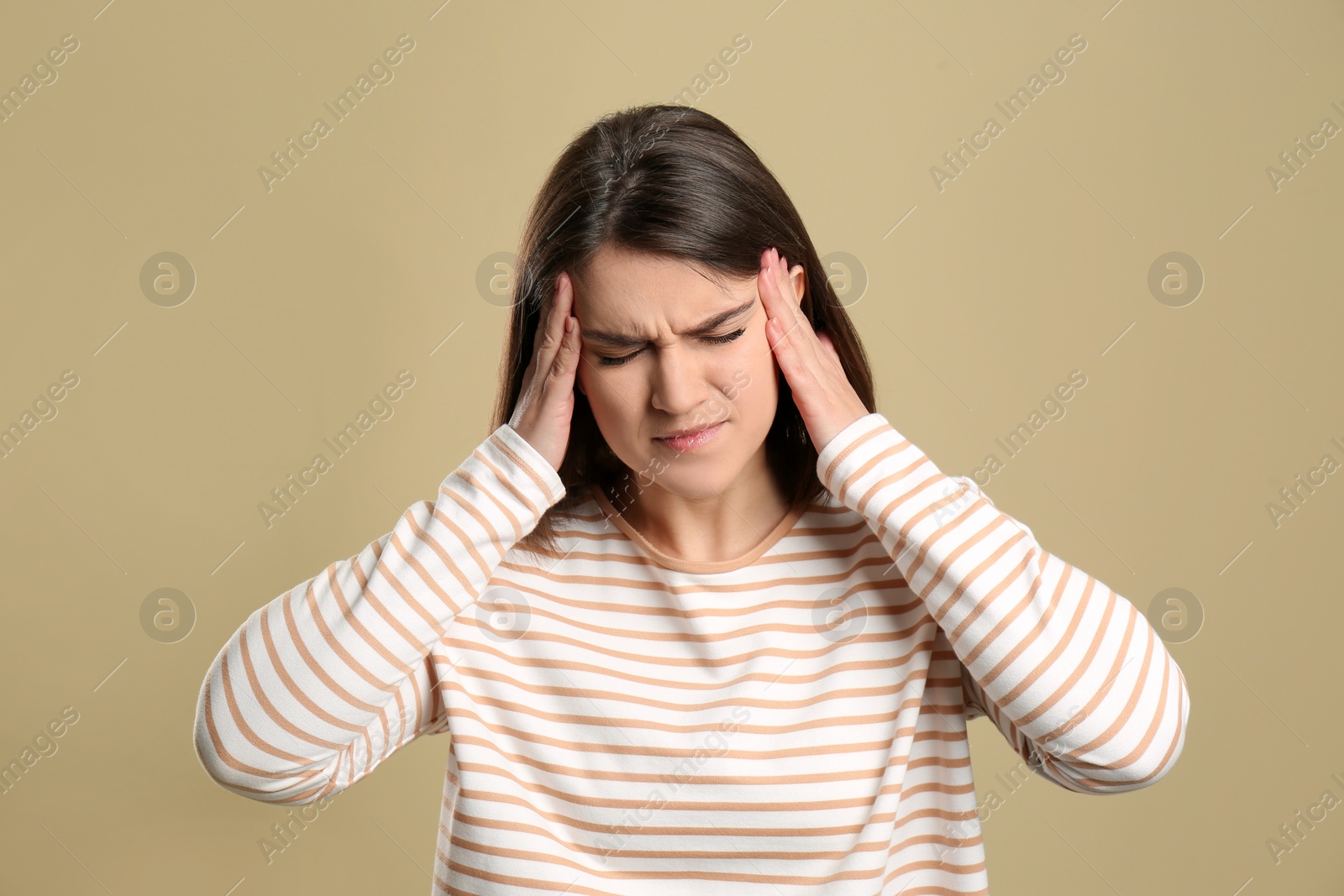 Photo of Young woman suffering from migraine on beige background