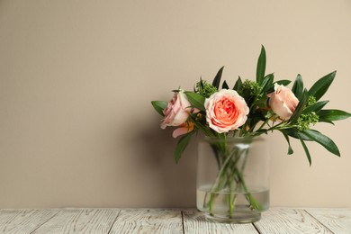 Bouquet with beautiful flowers in glass vase on light wooden table against beige background. Space for text