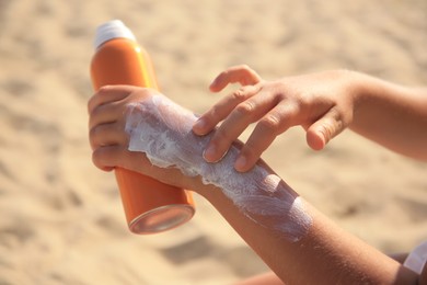 Photo of Child applying sunscreen on sandy beach, closeup. Sun protection care