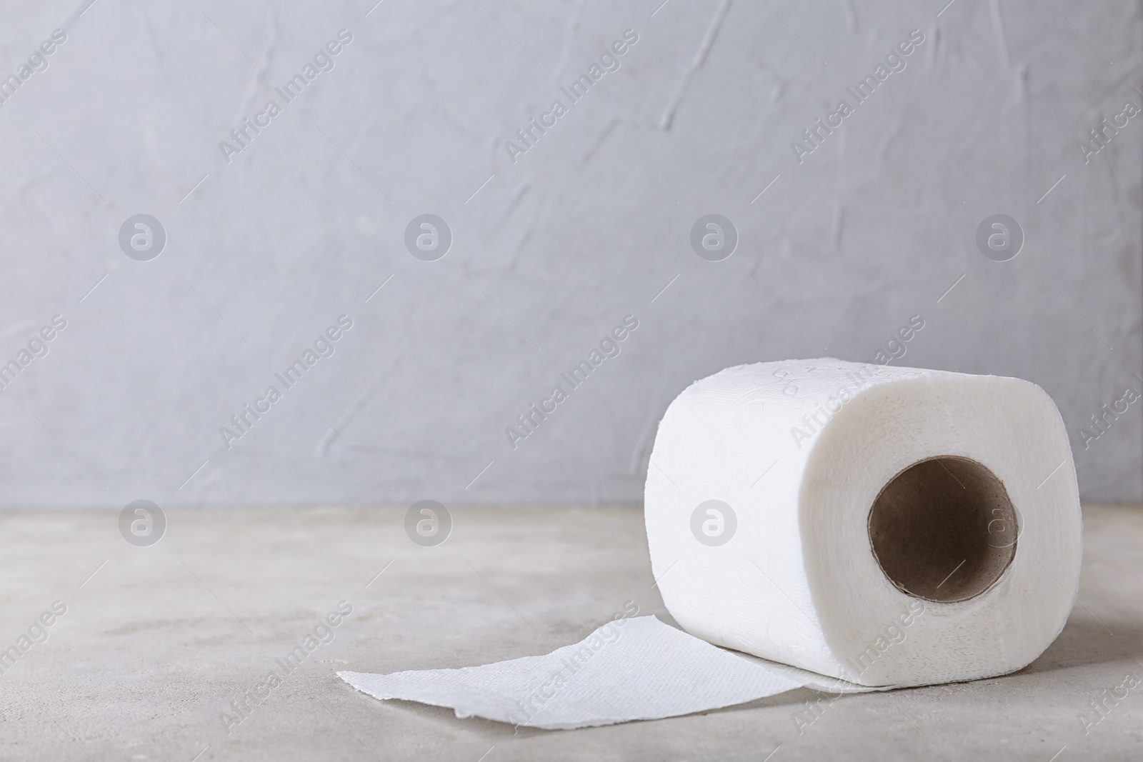 Photo of Roll of toilet paper on grey table. Space for text