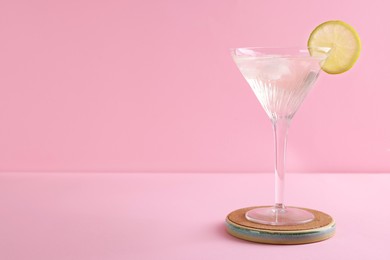 Photo of Martini glass of cocktail with lemon slice on stand against pink background. Space for text