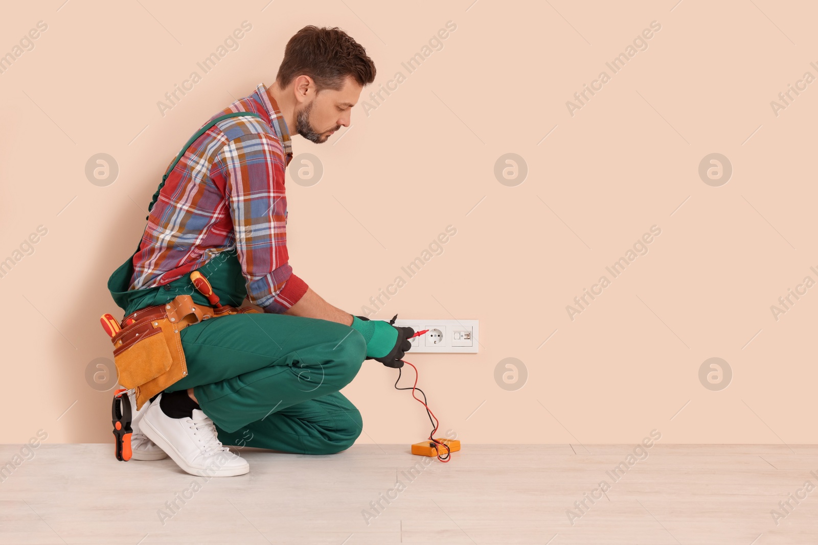 Photo of Electrician in uniform with tester checking voltage indoors. Space for text