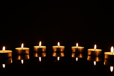 Burning candles on mirror surface in darkness, space for text