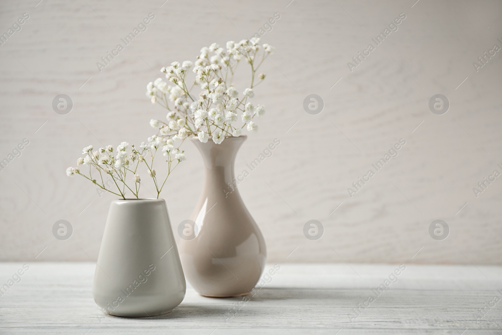 Photo of Gypsophila flowers in vases on table against light background. Space for text