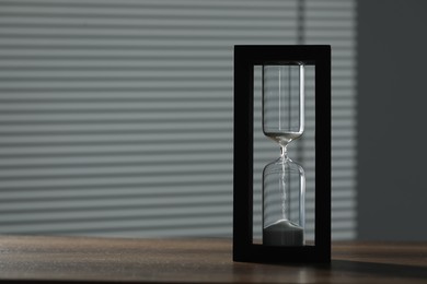 Photo of Hourglass with flowing sand on wooden table, space for text