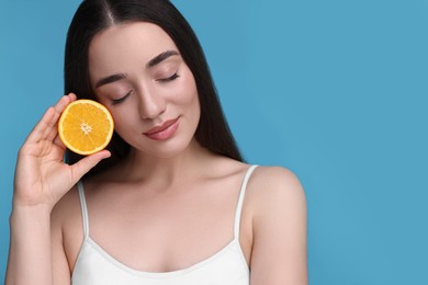 Photo of Beautiful young woman with piece of orange on light blue background. Space for text