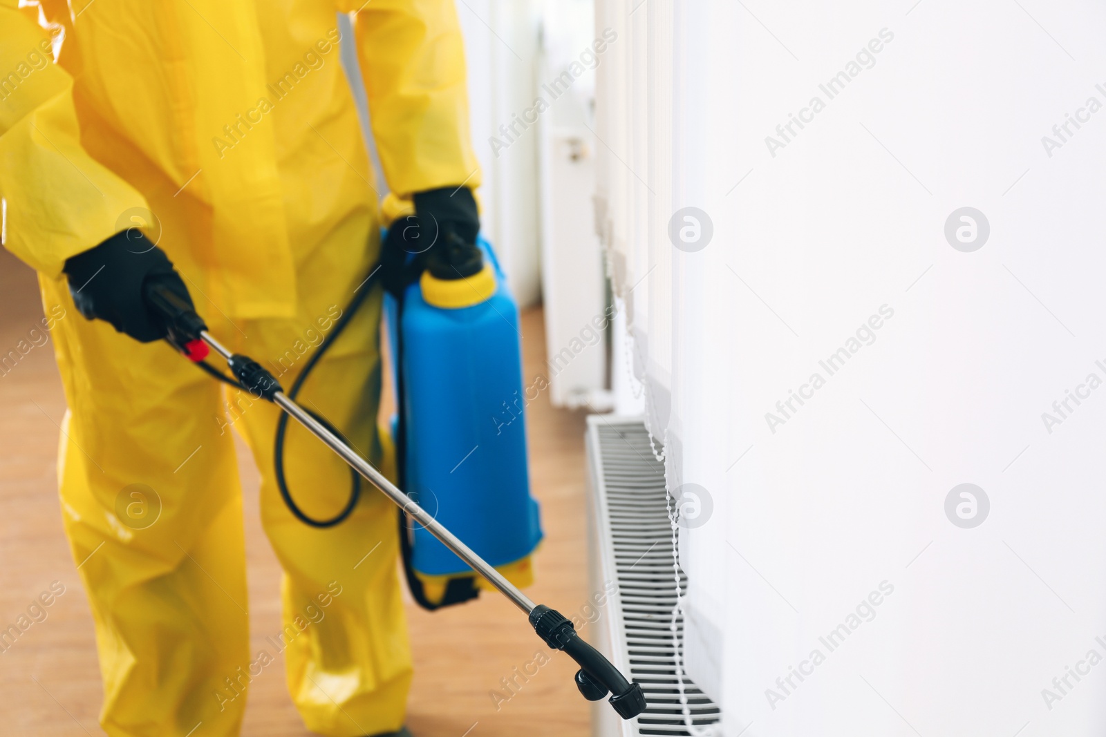 Photo of Pest control worker in protective suit spraying pesticide indoors, closeup. Space for text
