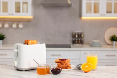 Photo of Making toasts for breakfast. Appliance, crunchy bread, honey, jam and orange fresh on white table in kitchen