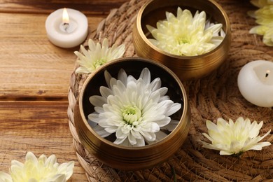 Photo of Tibetan singing bowls, beautiful chrysanthemum flowers and burning candles on wooden table, closeup