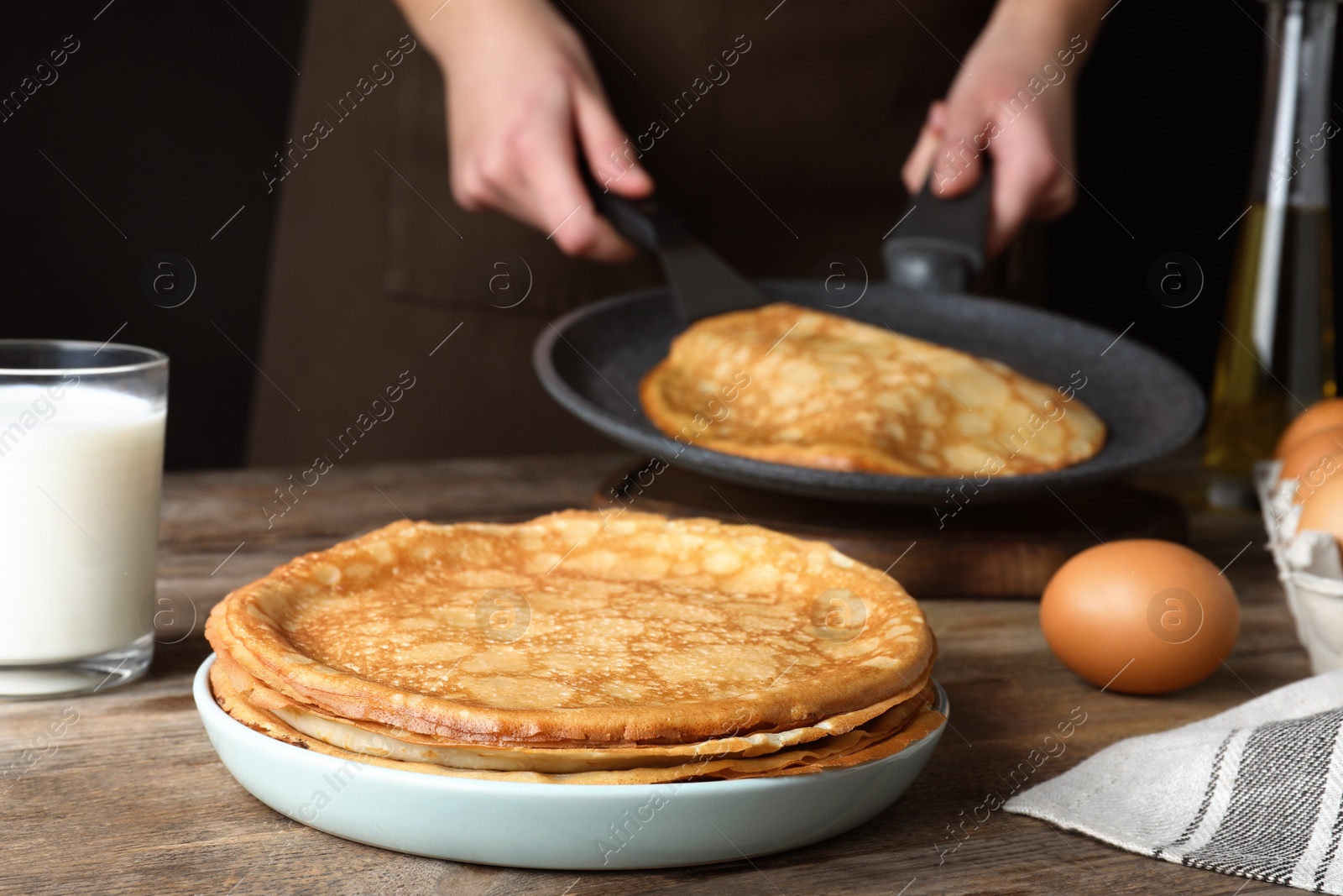 Photo of Woman cooking delicious thin pancakes at wooden table