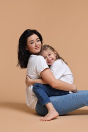 Photo of Beautiful mother with little daughter sitting on beige background