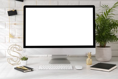 Photo of Office workplace with computer, stationery and decor on light table near white brick wall