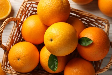 Photo of Many ripe oranges and green leaves on wooden table, top view