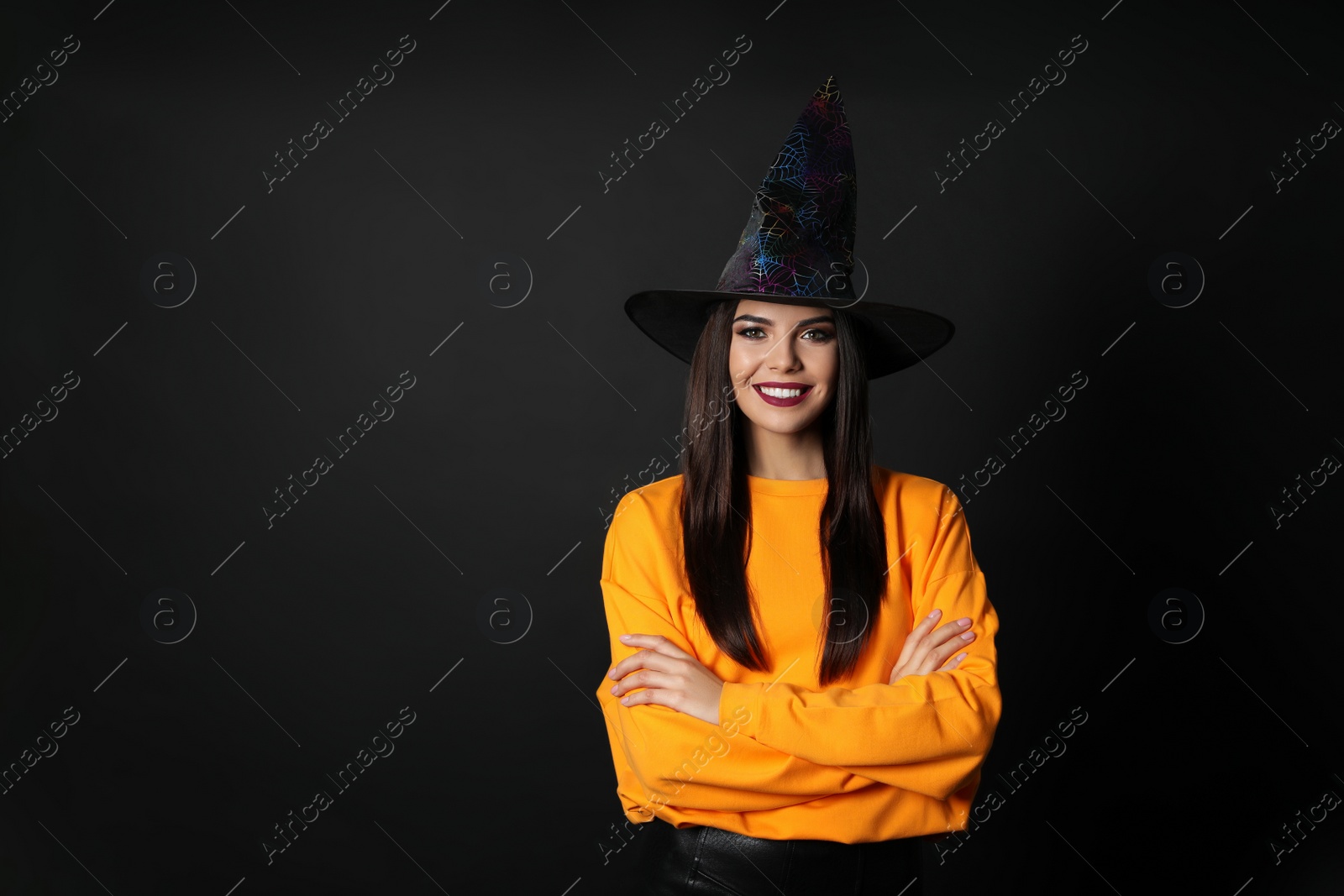 Photo of Beautiful woman wearing witch costume for Halloween party on black background, space for text