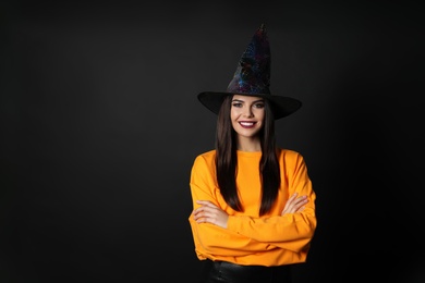 Photo of Beautiful woman wearing witch costume for Halloween party on black background, space for text