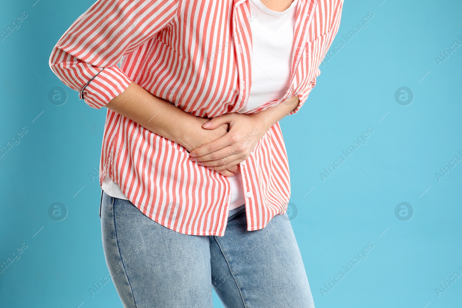 Photo of Woman suffering from stomach ache on light blue background, closeup. Food poisoning