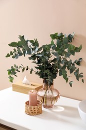 Vase with eucalyptus branches and burning candle in bathroom. Interior design