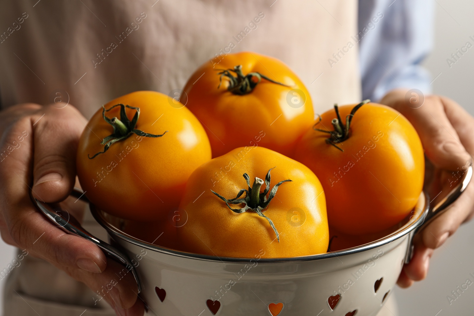 Photo of Woman holding colander with fresh ripe yellow tomatoes, closeup