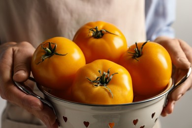 Photo of Woman holding colander with fresh ripe yellow tomatoes, closeup