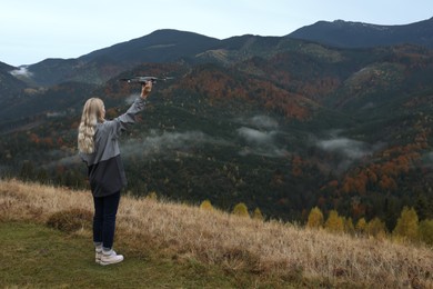 Photo of Young woman with modern drone in mountains, back view. Space for text