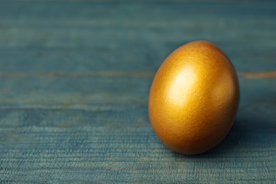 Golden egg on light blue wooden table, closeup. Space for text