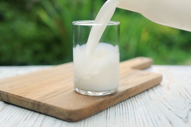 Photo of Pouring tasty fresh milk into glass on white wooden table, closeup