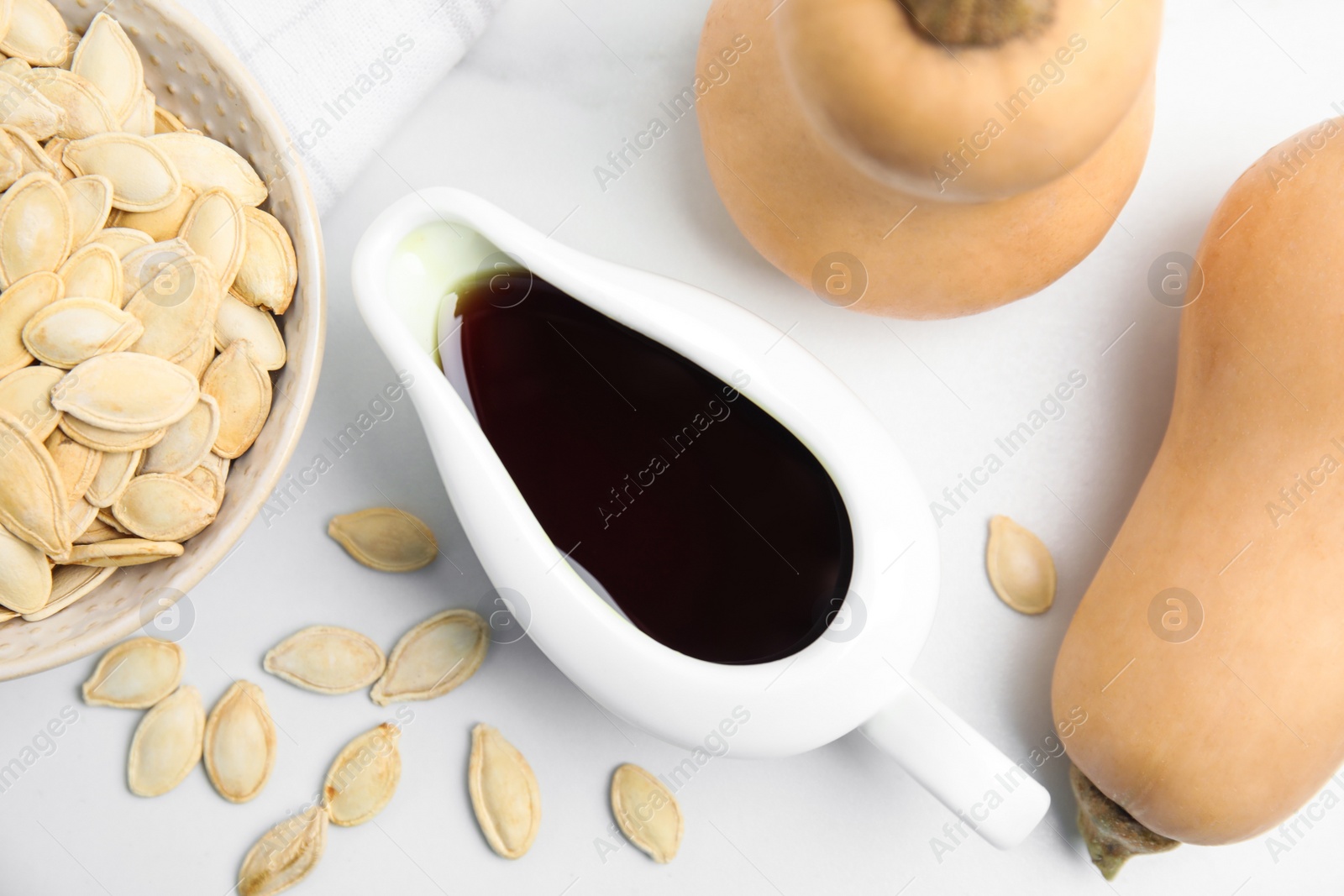 Photo of Gravy boat of oil, pumpkins and seeds on white table, flat lay