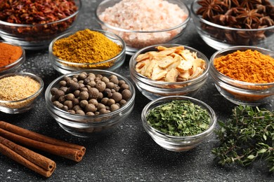 Photo of Glass bowls with different spices on grey textured table, closeup
