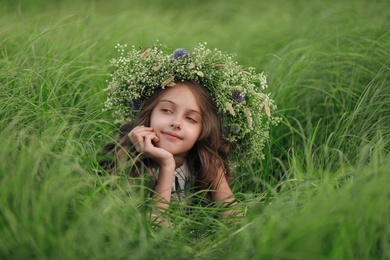 Cute little girl wearing wreath made of beautiful flowers in field