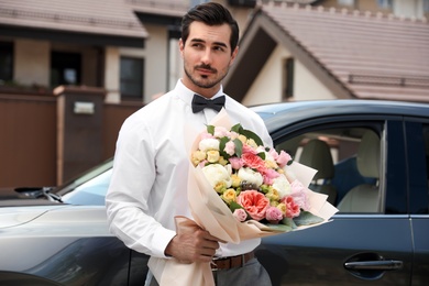 Young handsome man with beautiful flower bouquet near car outdoors