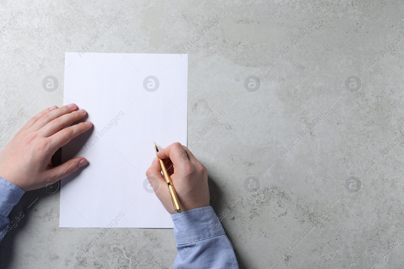 Photo of Man writing on sheet of paper with pen at light grey table, top view. Space for text