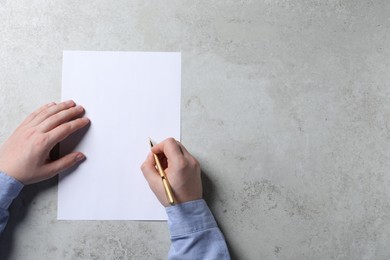 Photo of Man writing on sheet of paper with pen at light grey table, top view. Space for text
