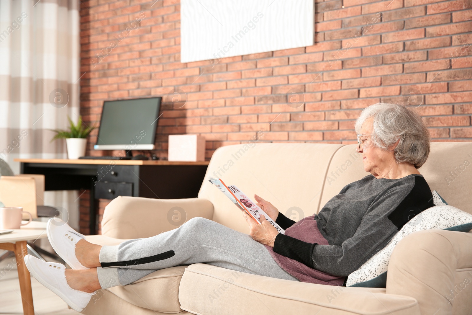 Photo of Elderly woman with magazine on sofa in living room