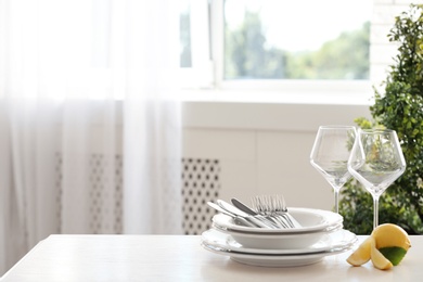 Photo of Set of clean dinnerware and lemon on table indoors. Space for text