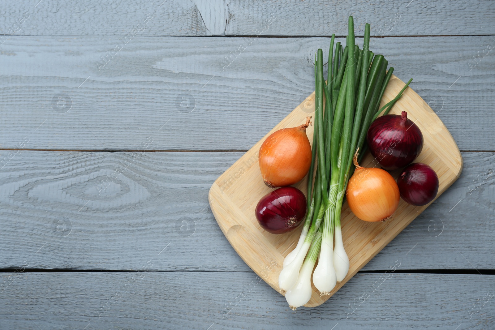 Photo of Board with different kinds of onions on grey wooden table, top view. Space for text