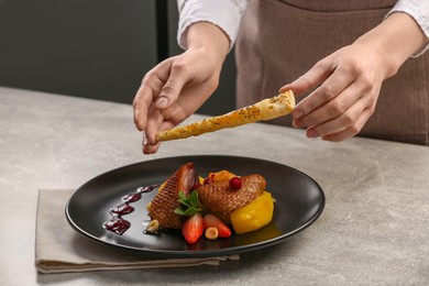 Food stylist preparing delicious dish with chicken, parsnip and strawberries for photoshoot at grey table in studio, closeup