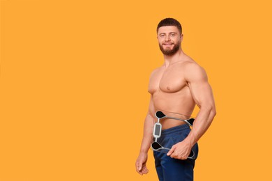 Photo of Portrait of happy athletic man with scales on orange background, space for text. Weight loss concept