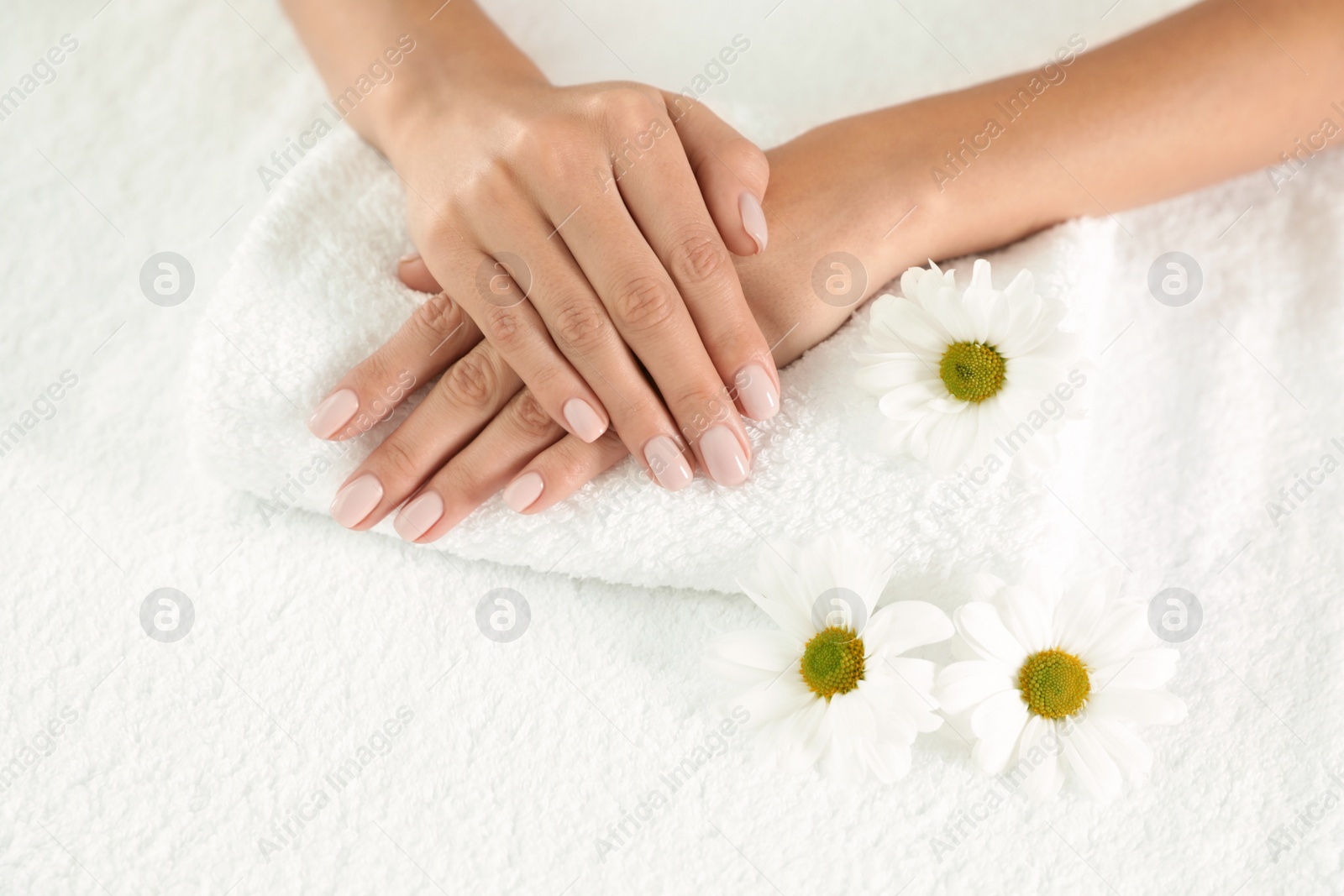 Photo of Woman with smooth hands and flowers on towel, closeup. Spa treatment